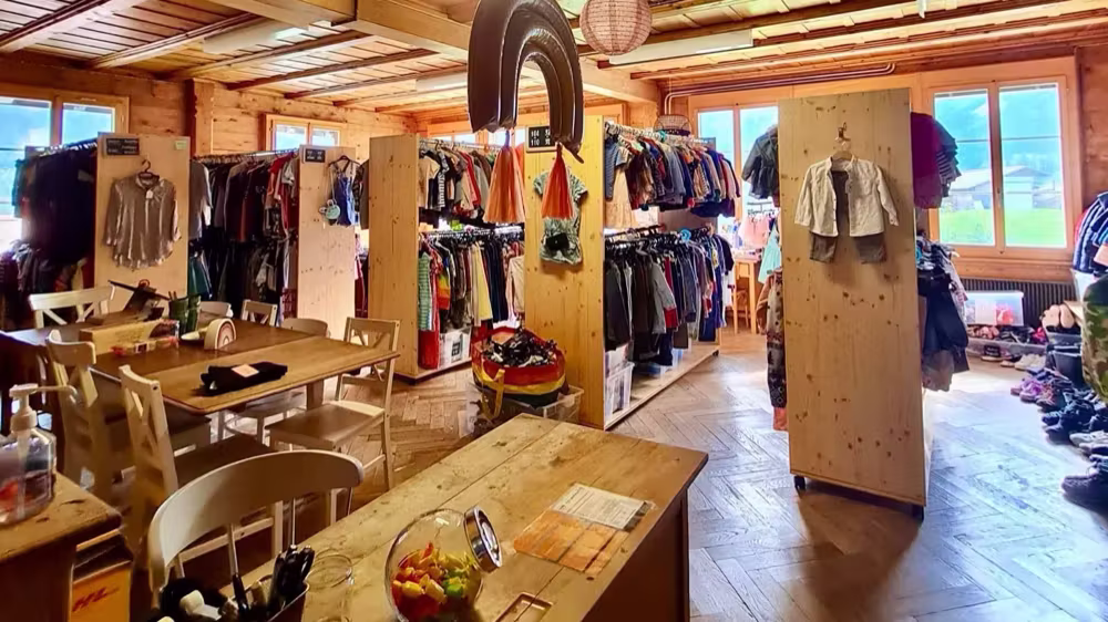 Der Laden im Schulhaus Itramen: Holzdecke, Kleiderständer und ein langer Tisch